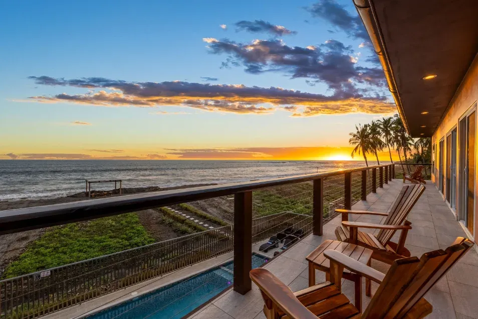Balcón con sillas Adirondack sobre la piscina al atardecer sobre el mar