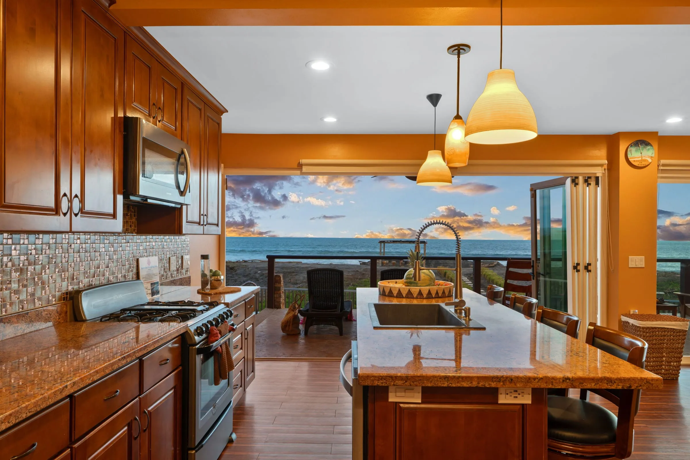 Cocina con isla y lámparas colgantes, con vista al mar por las puertas abiertas