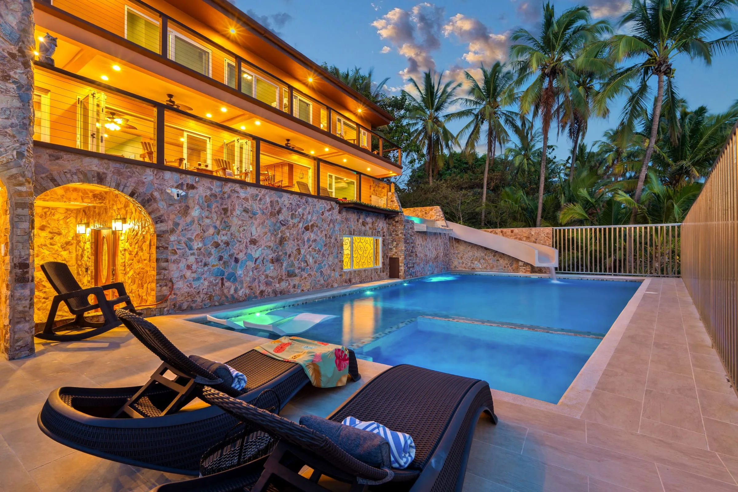 Terraza de la piscina con camastros bajo los arcos de piedra de la casa al anochecer