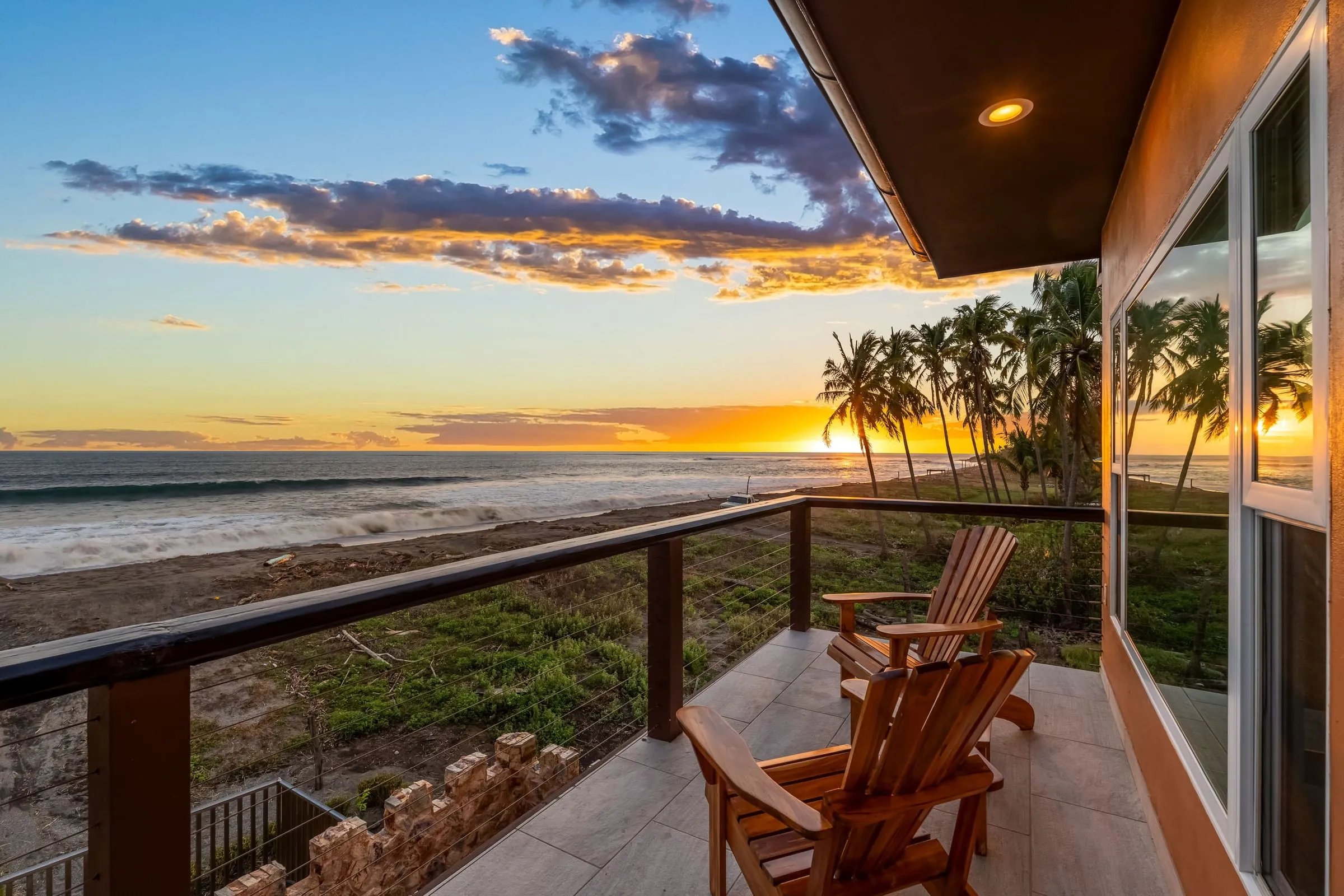 Terraza superior con sillas sobre la playa y las palmeras al atardecer