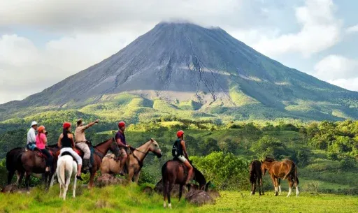 Jinetes a caballo en un potrero bajo un volcán