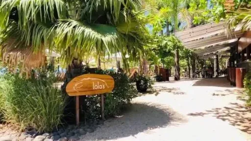 Rótulo de Lola's en un sendero de arena entre palmeras