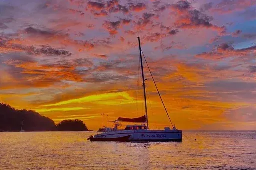 Un catamarán en agua tranquila bajo un cielo naranja al atardecer