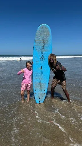 Dos niños con una tabla de surf en la orilla