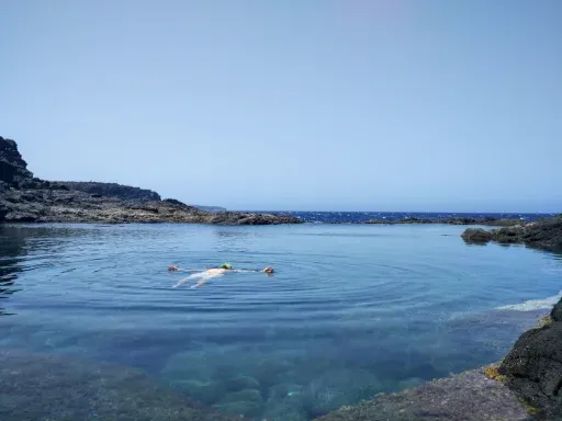 Una persona flotando en una poza rocosa tranquila junto al mar